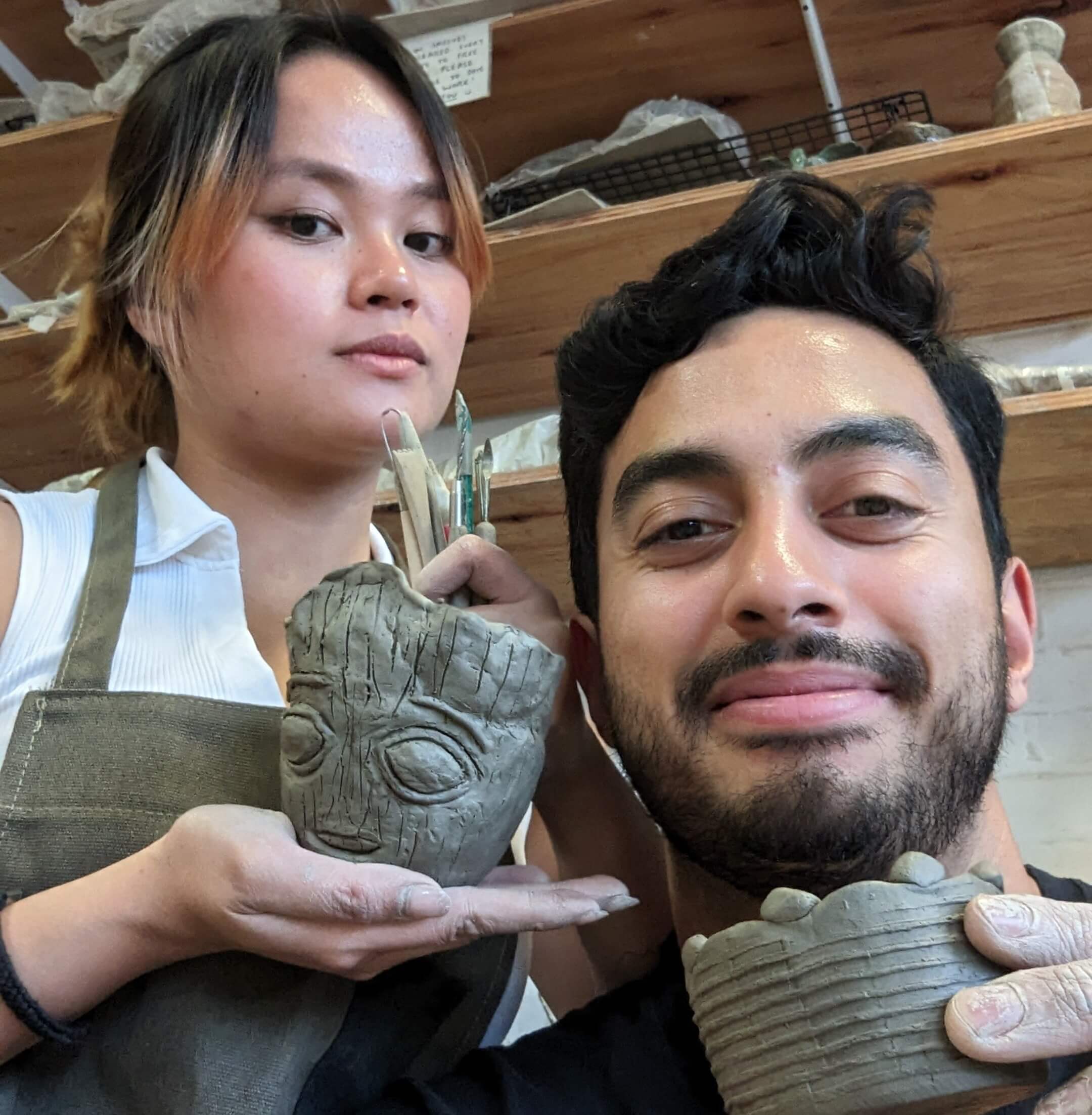 A couple holding ceramic sculptures in a workshop setting.
