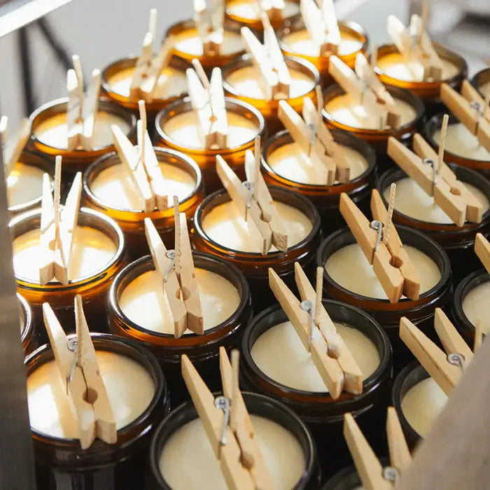 Small candles in amber jars with wooden clothespins on top, arranged in rows.
