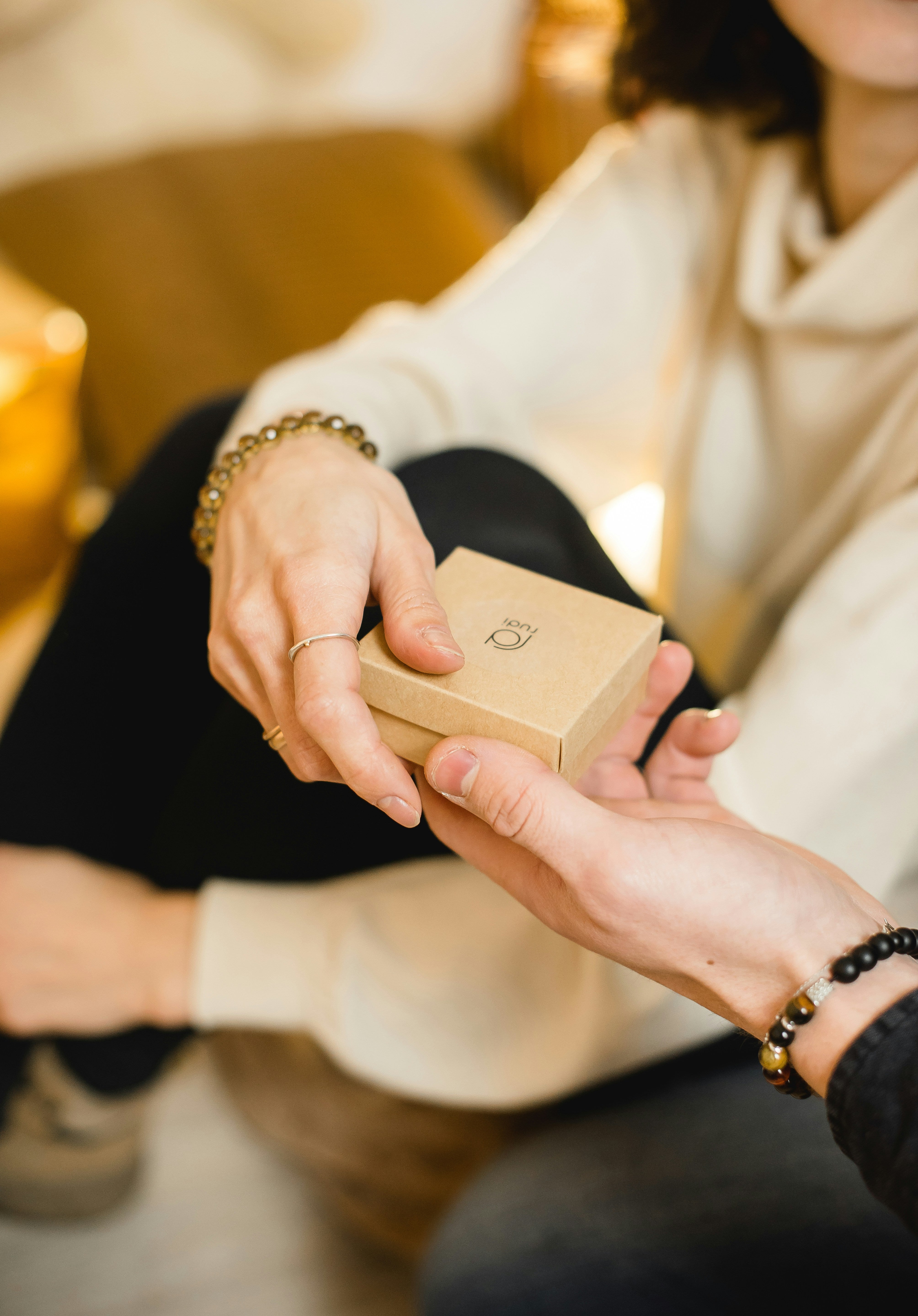 Person holding a small gift box with another person's hand, in a warm indoor setting.
