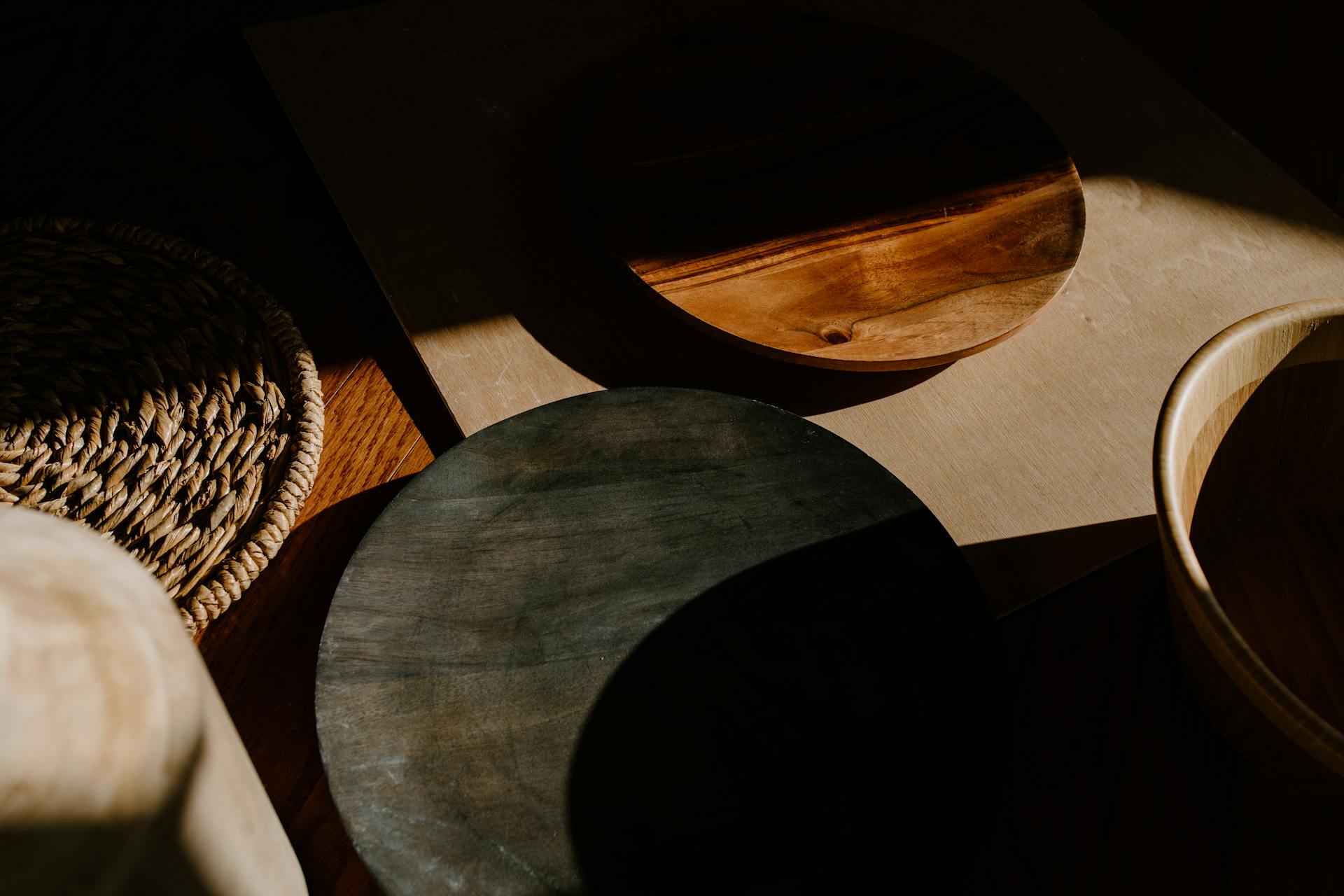 Wooden plates and a woven mat on a dark, shadowy, wooden surface.