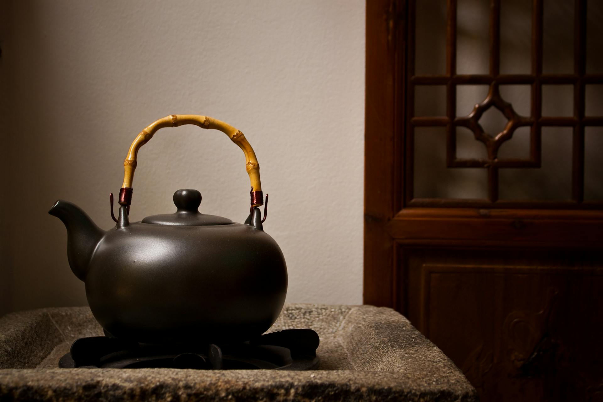 Black teapot with a yellow handle on a stone surface, traditional setting.