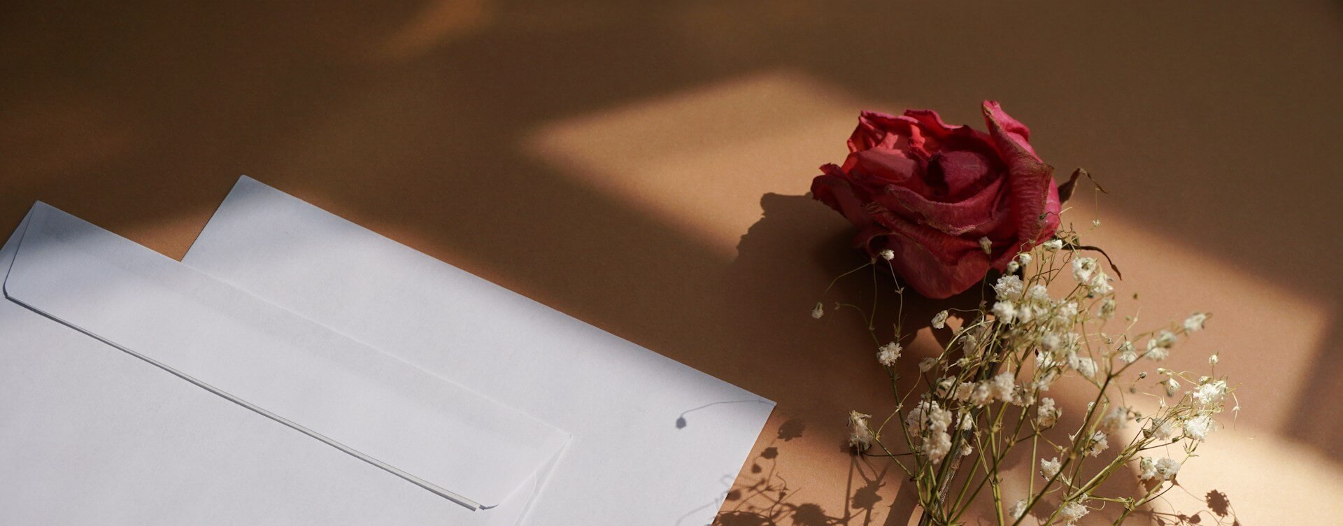 Red rose and white envelope on a textured surface with soft lighting